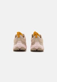 Beige idrettssko med rosa såle og gul hæltrekk. Teksturert materiale med lagdelt design og mønstret yttersåle.