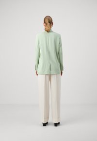 Blazer entallado color verde menta con una abertura trasera, combinado con pantalones crema de cintura alta y botas negras hasta el tobillo. Textura suave.
