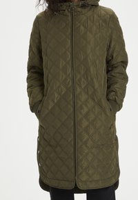 Manteau matelassé vert olive avec fermeture éclair à l'avant, capuche et boutons-pression sur les côtés ; présente un motif en losanges et des poignets côtelés.