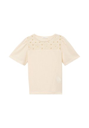 Blouse crème à manches courtes avec encolure ronde et détails en dentelle crochetée sur la partie supérieure de la poitrine et les épaules.