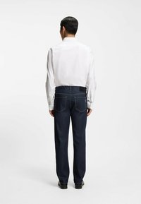 Valkoinen pitkähihainen paita, jossa on napilliset kalvosimet, yhdistetty tummiin denim-housuihin, joissa on takataskut ja kontrastitikkaukset.