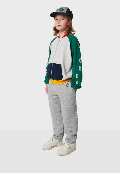 Färgglad zip-up jacka med grå, grön och marinblå paneler, ihopparad med vadderade grå byxor och vita sneakers. Kappan är mörkblå med text.