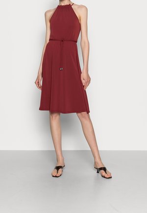 Bordeauxfarbendes Halterneck-Kleid mit gerafftem Ausschnitt, geflochtenem Taillengurt und A-Linien-Form. Model trägt flache, braune Sandalen. Glatte Stofftextur.