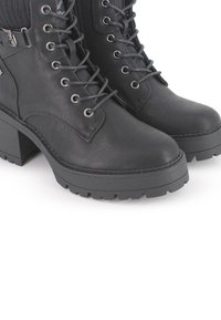 Botas negras hasta el tobillo en cuero sintético con un acabado texturizado, que presentan ojales metálicos, cordones y una suela gruesa y dentada.