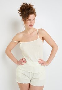 Ensemble deux pièces de couleur beige clair à côtes, comprenant un débardeur à fines bretelles et un short à volants avec une finition texturée.