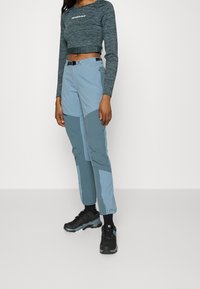 Ljusblå kort topp med grå detaljer, tillsammans med ljusblå smalbyxor med mörkare knäpartier, och svarta sneakers.