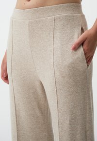 Beige wijde broeken van zacht materiaal, met een gestructureerd oppervlak, zijzakken en een aangesloten tailleband met subtiele stikseldetails.