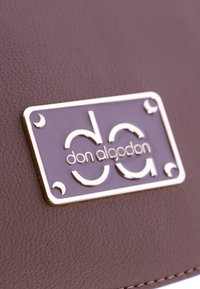 Bolso de piel sintética marrón con un logo rectangular con acentos dorados que presenta el texto "don algodón" y detalles curvos distintivos.