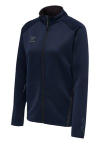 Mörkblå zip-jacka i mjukt tyg, med ståkrage, sidfickor och subtil logodetalj på bröstet och ärmen.