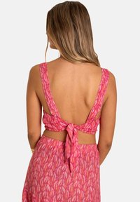 Vestido rosa con detalle de lazo en la espalda, que presenta un patrón floral. La tela parece ligera con una textura suave. Diseño de tirantes finos.