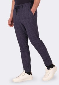 Pantaloni a righe blu navy con vestibilità rilassata, dotati di una cintura elastica e tasche laterali, abbinati a scarpe da ginnastica bianche.