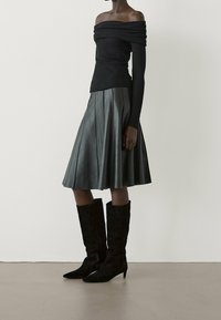 Top nero off-the-shoulder, gonna di pelle plissettata e stivali alti fino al ginocchio in suede nero con punta appuntita. Texture liscia e design aderente.