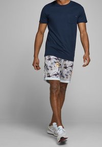 Tmavě modré bavlněné tričko s kapsou na hrudi, kombinované s bílými šortkami s květinovým vzorem a bílými sportovními botami.