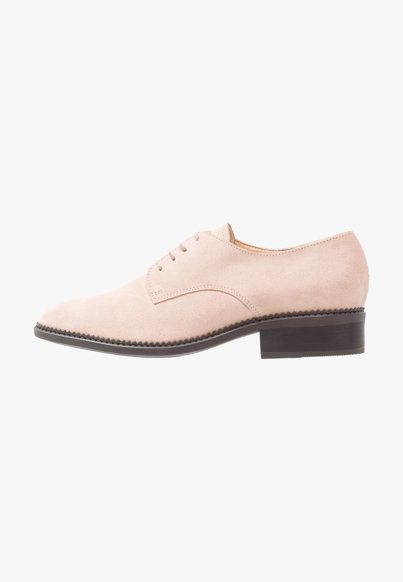 Chaussure Oxford en daim beige clair avec laçage fermé, détails de couture et un petit talon empilé de couleur brun foncé.