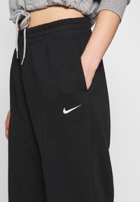 Black Nike sweatpants with an elastic waistband, side pockets, and a white logo on the left thigh. Made from soft jersey material.