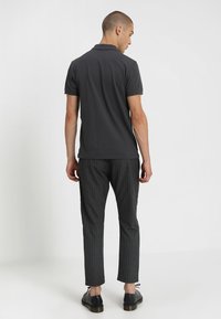 Dunkelgraues Poloshirt für Herren mit kurzen Ärmeln, kombiniert mit schwarzen gestreiften Hosen und schwarzen Schuhen. Schlichtes Design, glatte Textur und taillierte Form.