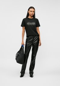 Melnā T-kreklā ar rhinestone logotipu, apvienots ar augsta vidukļa melnām mākslīgās ādas biksēm. Redzama melna somiņa ar zilu rokturi.