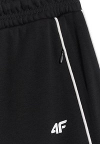Pantalon de sport noir avec ceinture élastique, liseré blanc sur les côtés, poche zippée et logo blanc "4F" près de la poche.