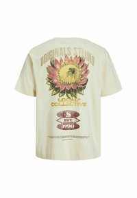 Krēmkrāsas kokvilnas T-kreklā ir liels saulespuķu grafiks uz muguras, pār kuru ir teksts "ORIGINALS STUDIO" un "LOCAL COLLECTIVE".