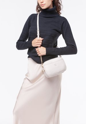 Borsa a tracolla in pelle testurizzata grigia chiara con hardware dorato e doppie zip, indossata con un dolcevita a coste blu navy e una gonna crema.