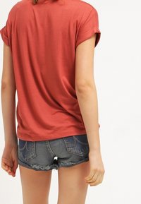 T-shirt couleur rouille avec des manches retroussées, associé à un short en denim taille haute avec des bords effilochés et des poches arrière.