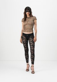Top trasparente con motivo mimetico e maniche corte, abbinato a leggings in pizzo nero con vita liscia e tacchi aperti neri.