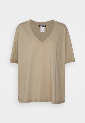 Beżowy bawełniany t-shirt z krótkim rękawem i dekoltem w serek z metką marki "HOPE" na kołnierzu, prezentowany na białym tle.