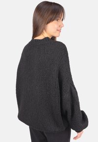 Schwarzer Strickpullover mit strukturierter, grober Optik. Verfügt über einen Rundhalsausschnitt und fallende Schultern. Locker sitzend mit langen Ärmeln.