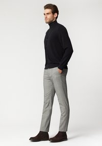 Czarny kardigan z guzikami na górze noszony z czarnym golfem, w połączeniu z szarymi spodniami w kratę i brązowymi botkami za kostkę. Gładki materiał, dopasowany krój.