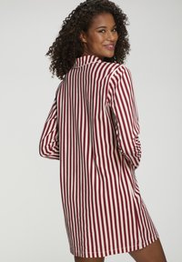 Svītraini kleita ar sarkaniem un baltajiem vertikālajiem līniju modeliem, garām piedurknēm, apkakles dizainu un brīvu piegriezumu. Teksturēts audums ar redzamām šuvēm.