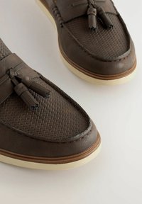 Mocassins en cuir brun avec une texture tissée, des accents de frange et des semelles en caoutchouc de couleur claire. Fini lisse avec des détails de surpiqûres contrastantes.