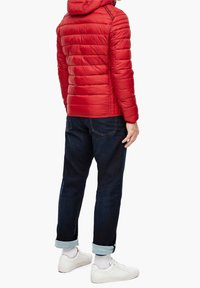 Doudoune rouge avec texture matelassée horizontale, capuche, associée à un jean bleu foncé à revers et des baskets blanches.