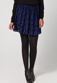 Gonna in pizzo nero con motivo floreale blu, vita arricciata e forma svasata. Abbinata a collant neri e stivaletti alla caviglia.