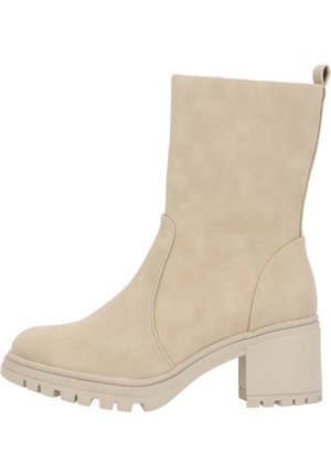 Bottine en daim beige avec un talon bloc, dotée d'un bout arrondi et de panneaux élastiques latéraux pour un enfilage facile. Semelle en caoutchouc texturé avec grip.