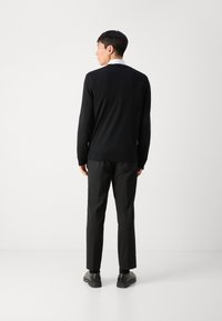 Suéter negro de punto con cuello redondo, combinado con pantalones negros. Textura suave, corte ajustado y sutiles acentos acanalados en el dobladillo.