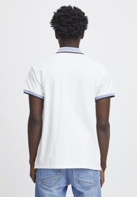 Weißes Poloshirt mit navyfarbenem Besatz am Kragen und an den Ärmeln, aus glattem Stoff, getragen mit blauen Jeans, zeigt ein schlichtes Design.