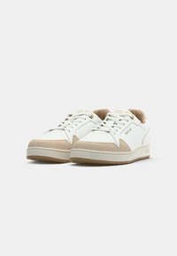 Baskets basses blanches avec des accents en daim beige, zone de bout perforée et logo "REPLAY" sur le côté et la languette.