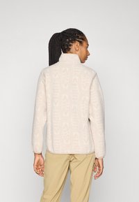 Fleece-Jacke in hellem Creme mit einem strukturierten geometrischen Muster, hohem Kragen und lässiger Passform. Lange Ärmel mit elastischen Bündchen.