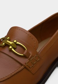 Mocassins en cuir marron avec un détail mors doré, une texture lisse et des surpiqûres sur le dessus. Design classique et forme élégante.