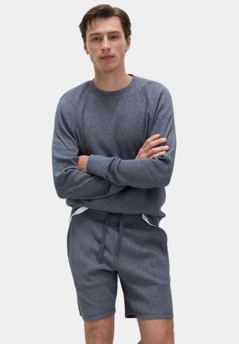 Szary bawełniany sweatshirt z rękawami raglanowymi, w połączeniu z pasującymi szortami z elastycznym pasem i szczegółem sznurkowym. Gładka faktura.