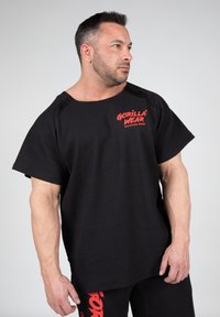 Zwarte textuurshortsleeve shirt met een rood "GORILLA WEAR" logo aan de voorkant, gecombineerd met bijpassende zwarte broek.
