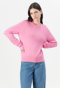 Roza pulover z dolgimi rokavi, okroglo ovratnico ter rebrastim robom in manšetami. V kombinaciji z svetlo modrimi ohlapnimi kavbojkami. Gladka tekstura.
