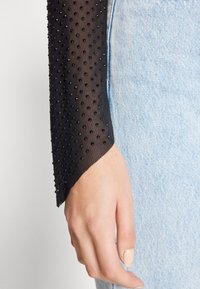 Svart genomskinlig nätärm med texturerade svarta pärlor. Kombinerad med ljusblå denim, vilket visar handens naturliga hudton och naglar.