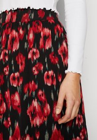 Gonna floreale nera con motivi rossi e turchesi. Tessuto morbido e strutturato con pieghe sottili e vita aderente. Top bianco a maniche lunghe con orlo arricciato.