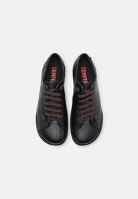 Paire de chaussures décontractées en cuir noir avec des lacets marron et un logo "Camper" rouge sur les semelles intérieures noires, vues de dessus sur fond blanc.