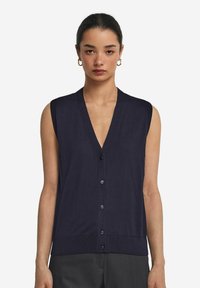 Mörkblå ärmlös cardigan med V-ringning, knäppning fram och ribbad kant. Tillverkad av ett mjukt tyg, med subtila stygnsdetaljer.