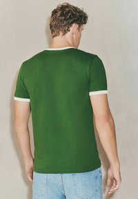Grøn kortærmet t-shirt med en hvid ribbet halsudskæring og ærmekanter, der har en tætsiddende pasform og glat tekstur.