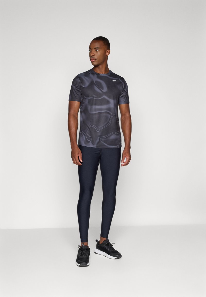 Korte mouwen zwart en grijs gemusterd sportshirt, gecombineerd met marineblauwe leggings en zwarte hardloopschoenen. Soepele stof, aansluitende pasvorm.
