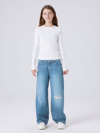 Tricou alb cu mânecă lungă și model rigat, asociat cu blugi largi decolorati, de un albastru deschis, și adidași albi. Ținută simplă și lejeră, cu texturi de bază.