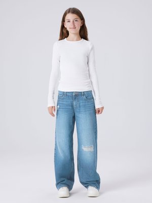 Valge pika varrukaga soonikkoesü, millele on sobitatud lahtised helesinised kulunud teksad ja valged spordijalatsid. Lihtne, šikk riietus koos põhitekstuuridega.